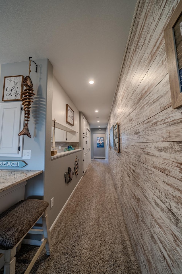corridor with baseboards, wood walls, recessed lighting, and carpet flooring