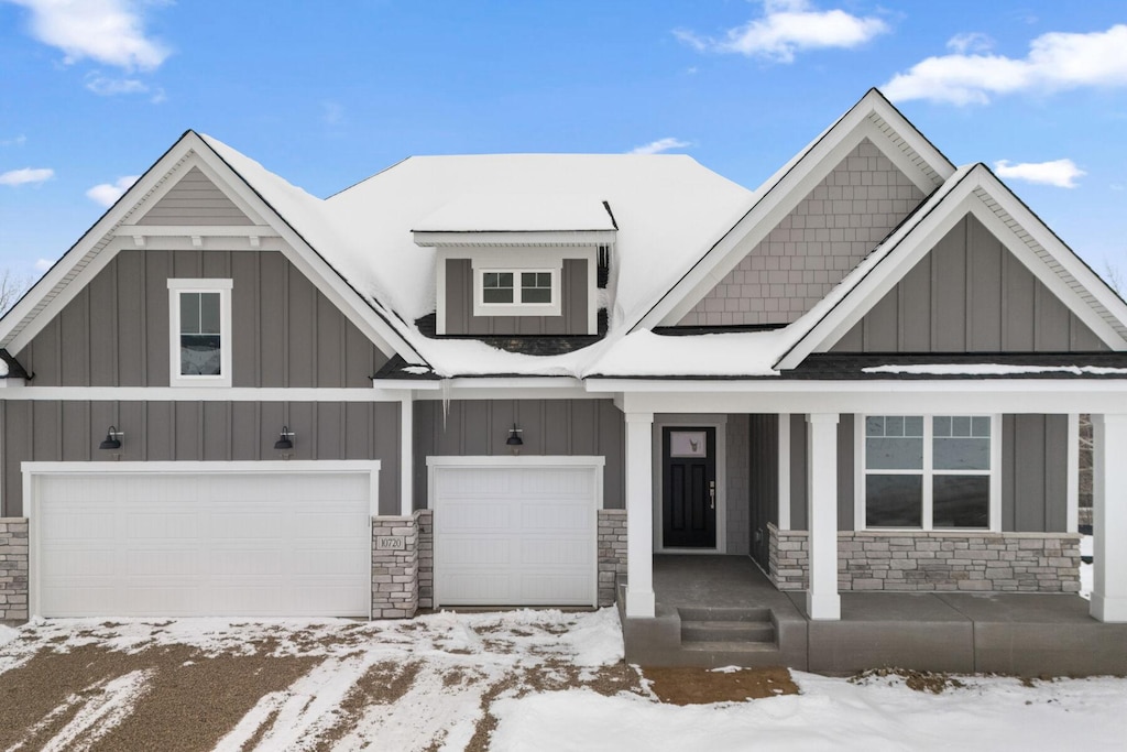 view of front of home with a garage, stone siding, covered porch, and board and batten siding