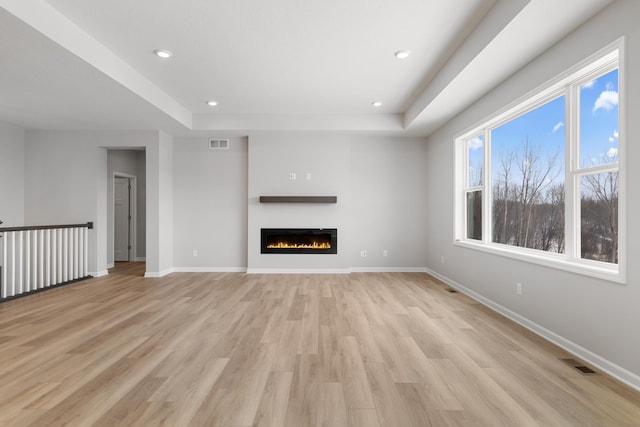 10720 Harbor Ln N, Maple Grove, MN 55369 - unfurnished living room with visible vents, light wood-style flooring, a raised ceiling, and a glass covered fireplace