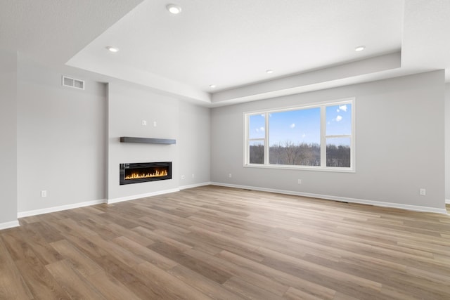 10720 Harbor Ln N, Maple Grove, MN 55369 - unfurnished living room featuring visible vents, light wood-type flooring, a glass covered fireplace, a tray ceiling, and recessed lighting