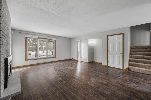 unfurnished living room featuring a brick fireplace, stairway, a textured ceiling, and wood finished floors