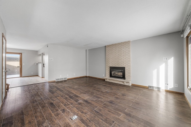 unfurnished living room with a brick fireplace, baseboards, visible vents, and wood finished floors