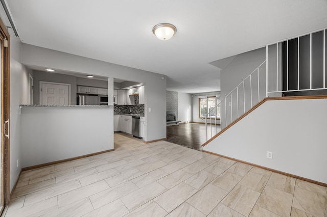 unfurnished living room featuring baseboards, a fireplace, and stairway