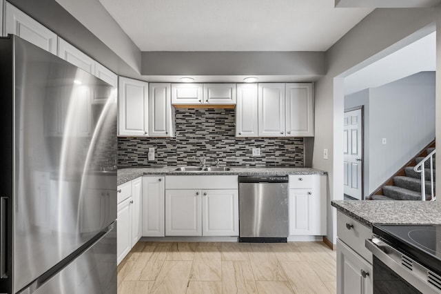 kitchen with appliances with stainless steel finishes, white cabinets, a sink, and decorative backsplash