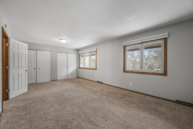 unfurnished bedroom featuring multiple closets, visible vents, carpet flooring, a textured ceiling, and baseboards