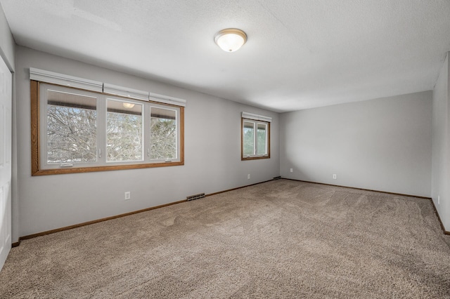 spare room with carpet, visible vents, a textured ceiling, and baseboards