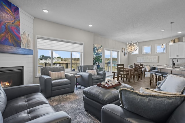 living room with a chandelier, a large fireplace, a textured ceiling, and wood finished floors