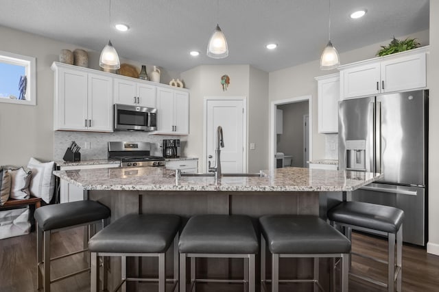 kitchen featuring light stone counters, stainless steel appliances, a sink, white cabinetry, and decorative backsplash