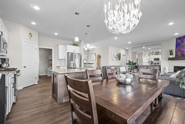 dining space with recessed lighting, dark wood-style flooring, a glass covered fireplace, and an inviting chandelier