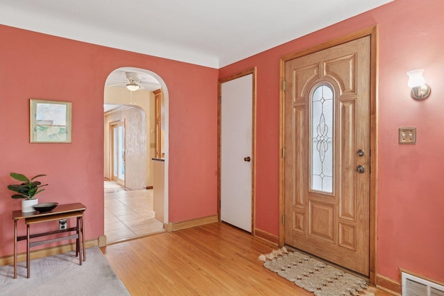 foyer featuring light wood finished floors, ceiling fan, visible vents, baseboards, and arched walkways