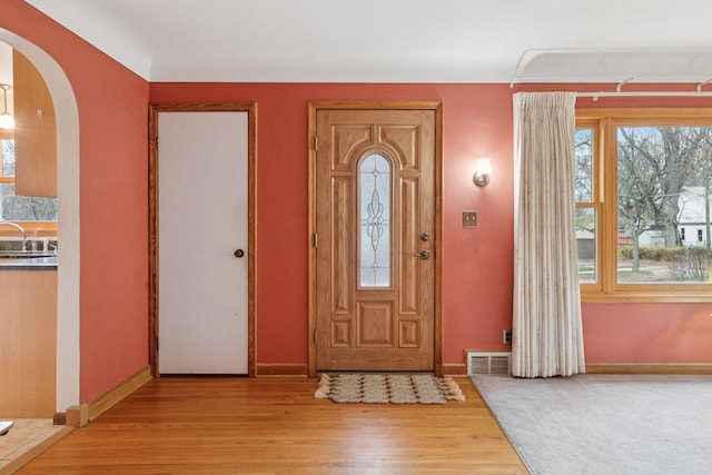 foyer with light wood-style floors, baseboards, visible vents, and arched walkways