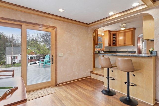 interior space featuring ornamental molding, arched walkways, ceiling fan, and light wood-style floors