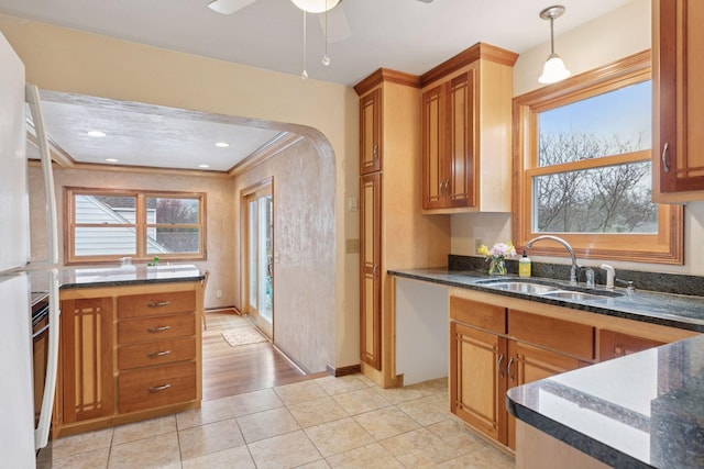 kitchen with dark stone countertops, a sink, brown cabinets, and a healthy amount of sunlight