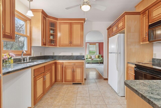 kitchen with dark stone countertops, a sink, arched walkways, black appliances, and a ceiling fan