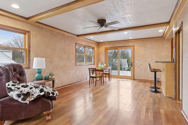 living area featuring crown molding, beamed ceiling, ceiling fan, baseboards, and wood finished floors