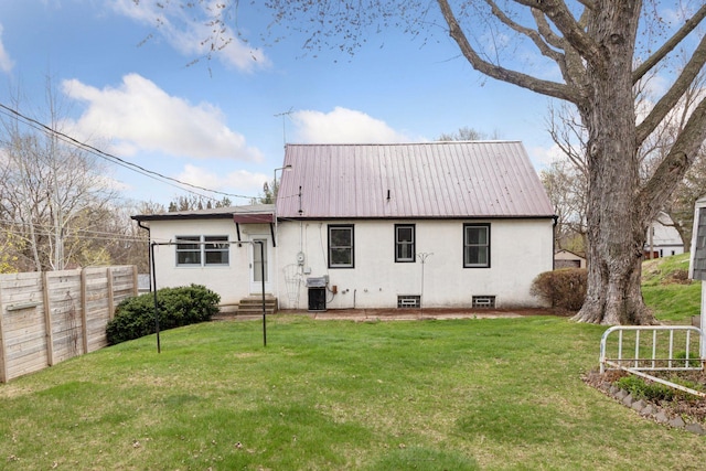 back of house featuring fence, entry steps, metal roof, stucco siding, and a yard