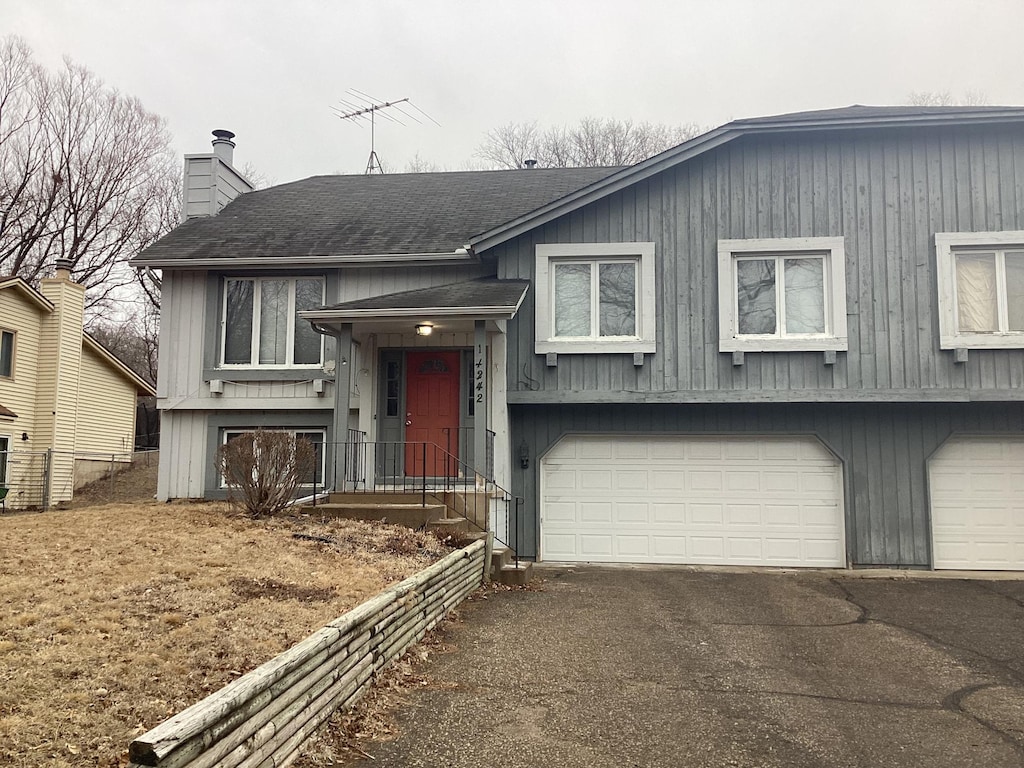 raised ranch with aphalt driveway, a chimney, a garage, and a shingled roof