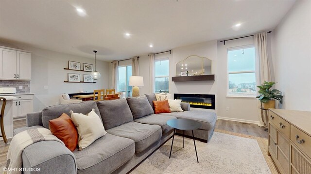 living room with baseboards, light wood-type flooring, a glass covered fireplace, and recessed lighting