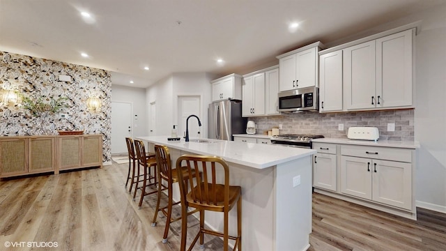 kitchen featuring light wood finished floors, stainless steel appliances, recessed lighting, a kitchen island with sink, and a sink