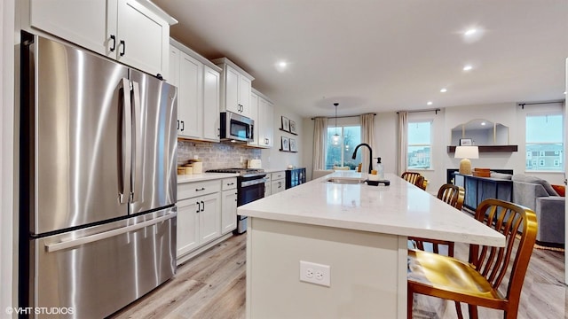 kitchen featuring a center island with sink, white cabinets, decorative backsplash, stainless steel appliances, and a sink