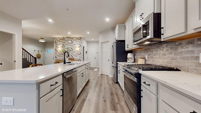 kitchen with stainless steel appliances, backsplash, white cabinets, a sink, and an island with sink