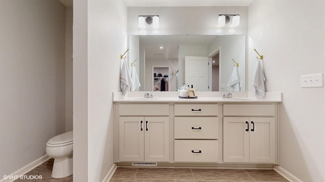 bathroom featuring double vanity, baseboards, visible vents, toilet, and a sink