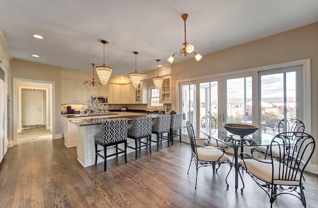 kitchen with dark wood-style floors, dark countertops, stainless steel microwave, glass insert cabinets, and a kitchen breakfast bar