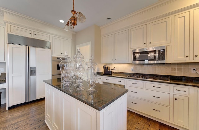 kitchen with dark stone counters, a kitchen island, appliances with stainless steel finishes, backsplash, and dark wood-style floors