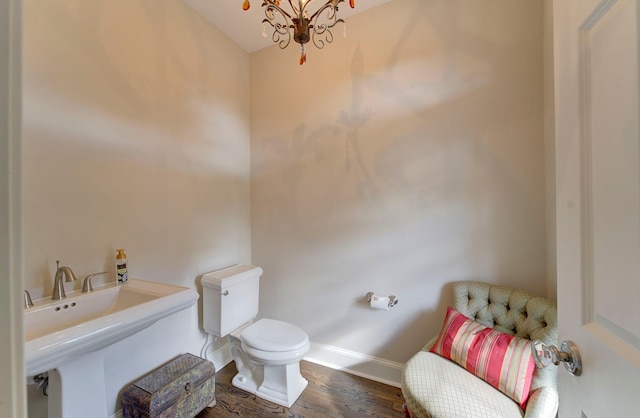 bathroom featuring toilet, a notable chandelier, a sink, wood finished floors, and baseboards