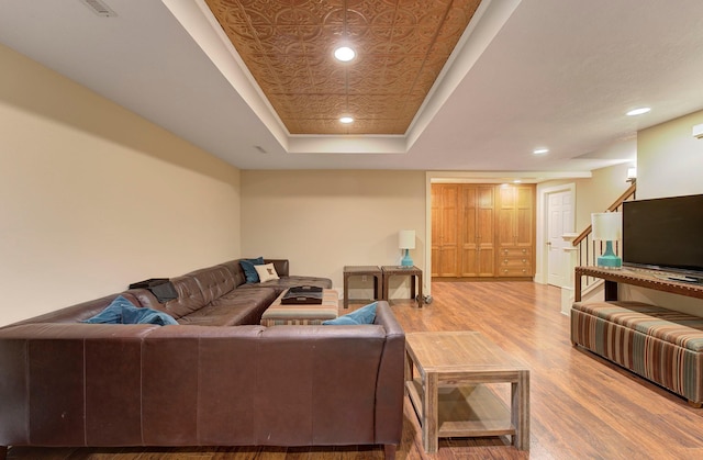 living room with stairs, a tray ceiling, wood finished floors, and recessed lighting