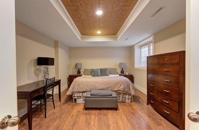 bedroom featuring a tray ceiling, baseboards, and wood finished floors