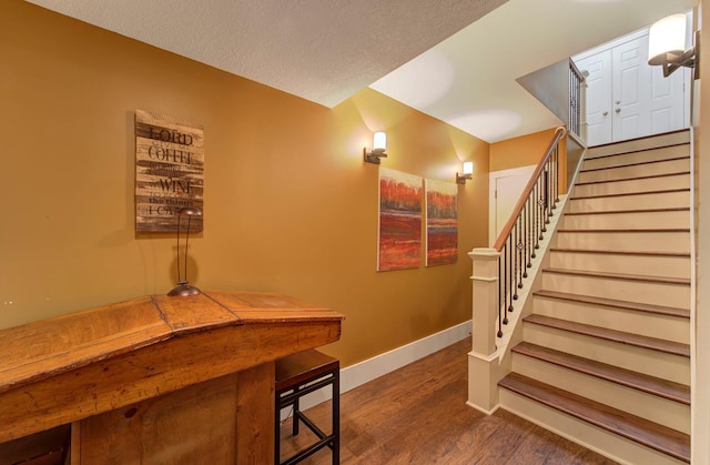 staircase featuring a textured ceiling, baseboards, and wood finished floors