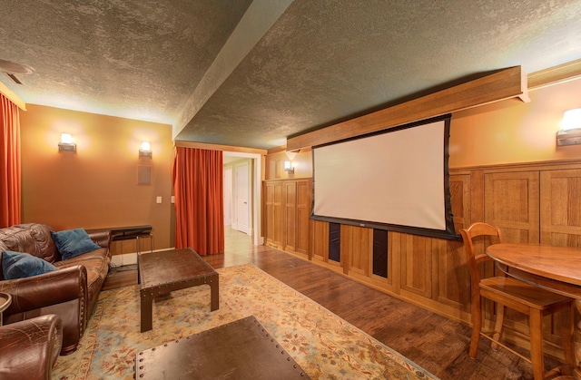 home theater room with wainscoting, a decorative wall, a textured ceiling, and wood finished floors