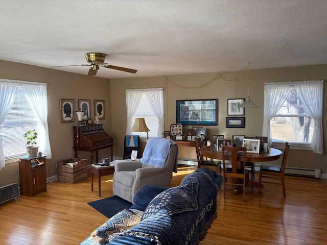 living area featuring a ceiling fan, a baseboard radiator, light wood-style flooring, and a textured ceiling