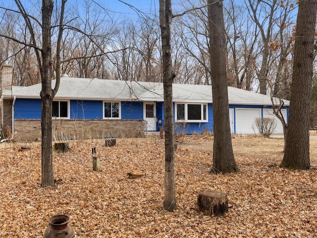 single story home featuring an attached garage, a chimney, and brick siding