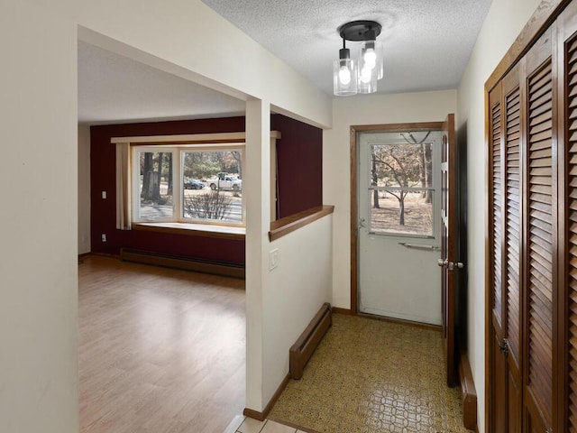 hall with baseboards, baseboard heating, a textured ceiling, and a chandelier