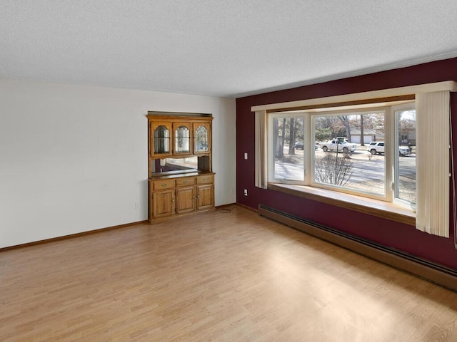 spare room with a textured ceiling, baseboard heating, light wood-type flooring, and baseboards