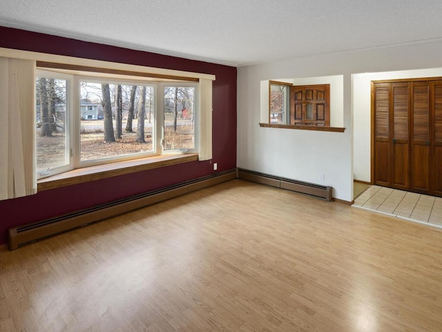 empty room featuring a textured ceiling, baseboard heating, light wood-style flooring, and baseboards