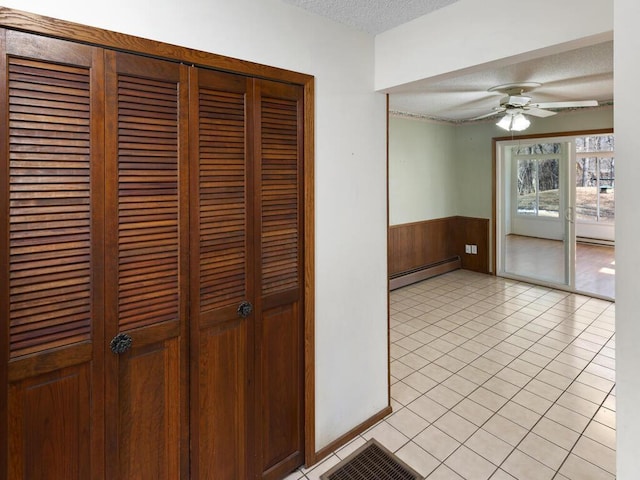 hall featuring light tile patterned floors, wooden walls, a wainscoted wall, a textured ceiling, and a baseboard heating unit