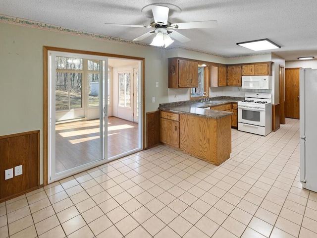 kitchen featuring a peninsula, white appliances, a sink, brown cabinetry, and dark countertops