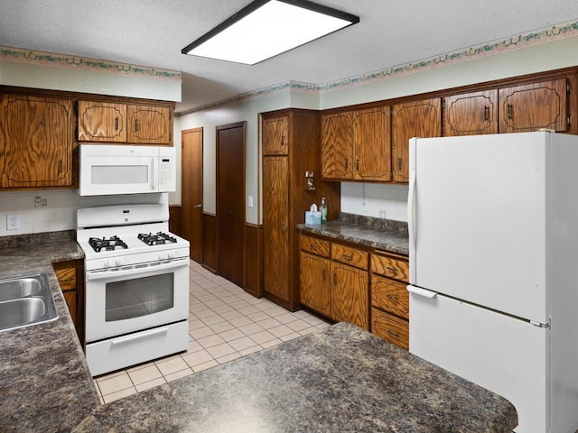 kitchen with dark countertops, white appliances, brown cabinetry, and light tile patterned flooring