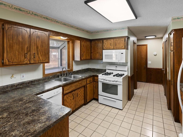 kitchen featuring white appliances, wainscoting, dark countertops, a textured ceiling, and a sink