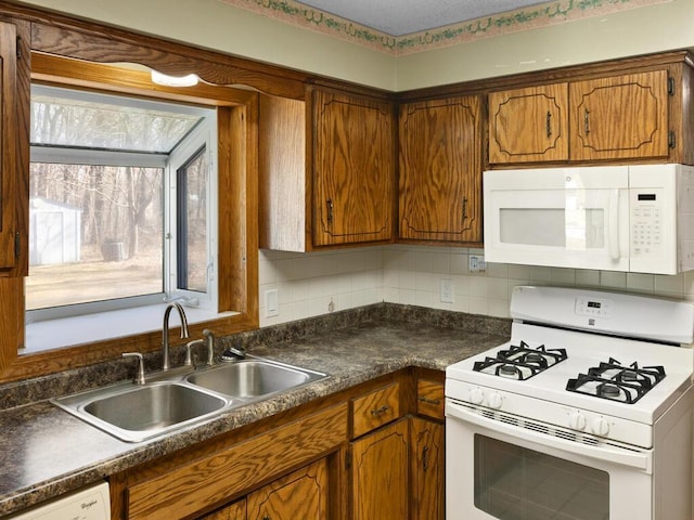 kitchen with white appliances, a sink, brown cabinets, tasteful backsplash, and dark countertops