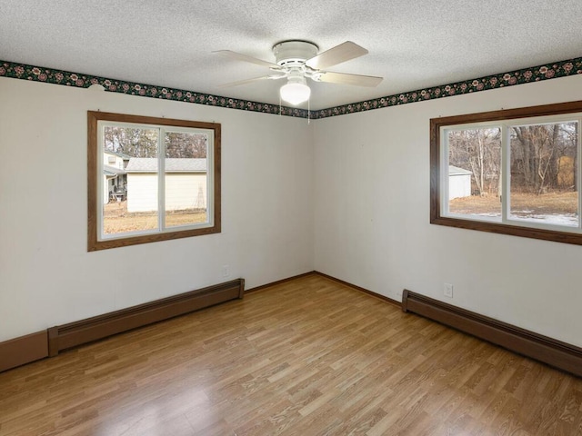 empty room featuring light wood-type flooring, baseboards, a textured ceiling, and baseboard heating