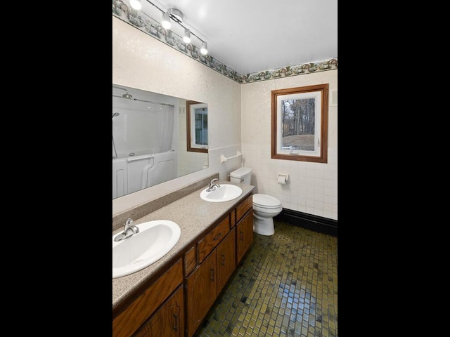 bathroom featuring tile patterned flooring, a sink, tile walls, and toilet