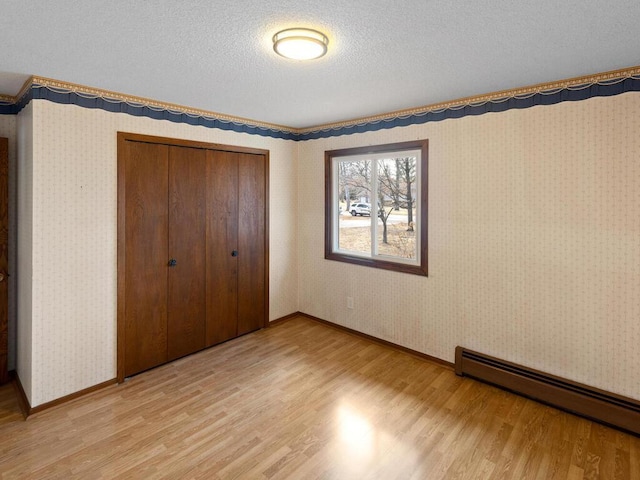 unfurnished bedroom featuring wallpapered walls, a baseboard radiator, a closet, and light wood-style floors