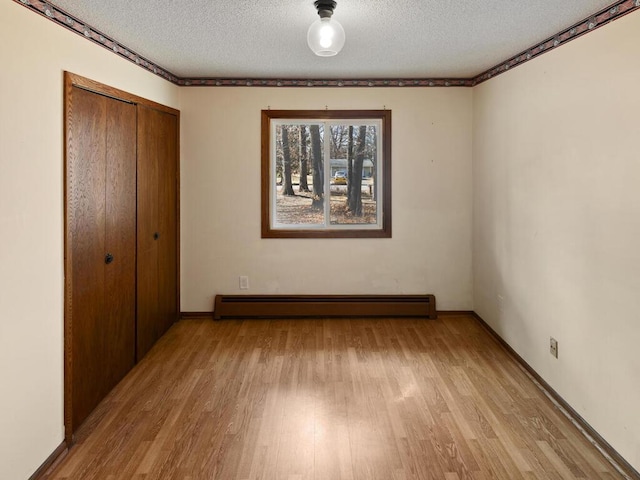 unfurnished bedroom with light wood finished floors, a closet, baseboard heating, a textured ceiling, and baseboards