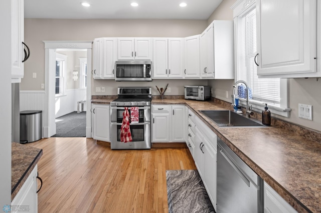 kitchen with appliances with stainless steel finishes, white cabinets, a sink, and light wood finished floors