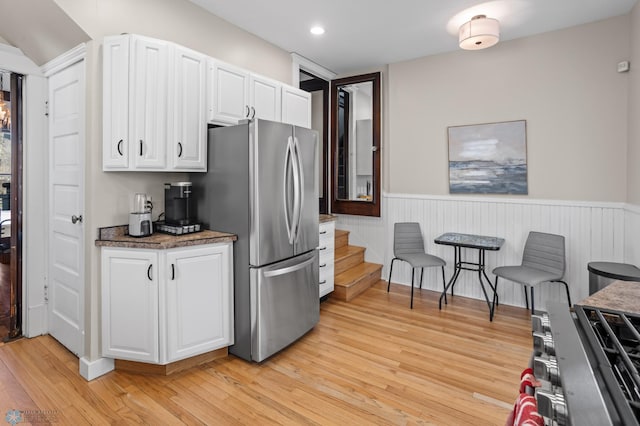 kitchen with light wood-type flooring, wainscoting, freestanding refrigerator, and white cabinetry