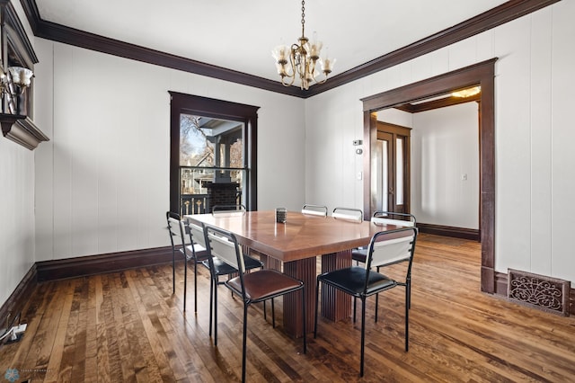 dining area featuring dark wood-style floors, baseboards, ornamental molding, and a notable chandelier